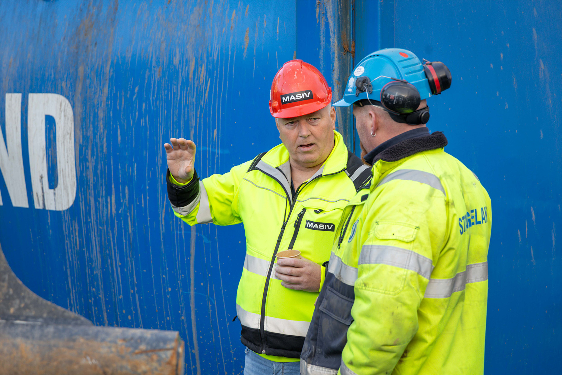 to menn i gul jakke og hjelmer foran en container